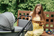 Maternity leave. Young mother studies, work or reads book with her newborn baby sleeps in stroller while walking in nature