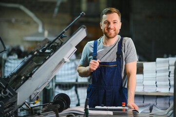 Portrait of production line worker controlling manufacturing process of modern packaging industrial machine in printing factory