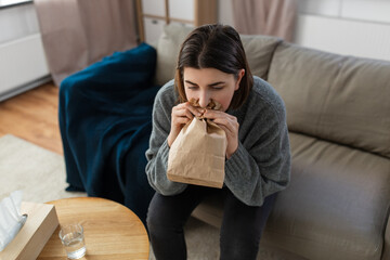 Wall Mural - mental health and psychological problem concept - woman having panic attack breathing to bag at home