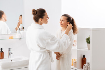 Sticker - beauty, hygiene, morning and people concept - happy smiling mother cleaning daughter's ear with cotton swab in bathroom