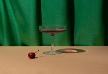 Champagne Glass, Cherry, Rich Green Drapery. Creative Fruity Cocktail Arrangement. 60s Vibes. 