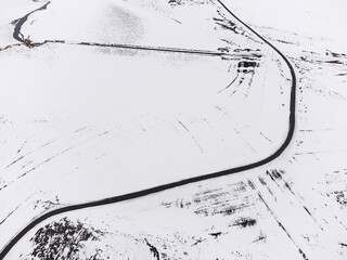 Aerial top view of a S shaped road with one lane and snow in winter