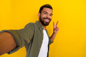 Wall Mural - Photo of excited funky guy dressed green shirt tacking selfie showing v-sign isolated yellow color background