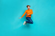 Full length photo of cute funky man wear orange pullover jumping high isolated teal color background