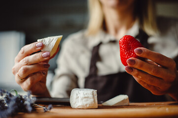 Piece of soft french cheese with white mold. Woman tasting camembert cheese with strawberries.