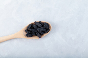 Black raisins in wooden spoon on grey background. Dried dehydrated grapes fruit. Selective focus, copy space