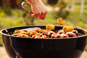 Wall Mural - man prepares a barbecue for friends, happy friends make a barbecue outdoors at sunset, A man roasts meat on the grill