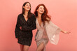 © Look! - Two beautiful young caucasian women in sparkly dresses are having party on pink background. Brunette and redhead are looking away smiling. Mood, lifestyle, concept.