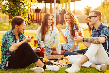 Wall Mural - group of friends are enjoying pizza in the park. Men and women sit on the grass around a pizza box