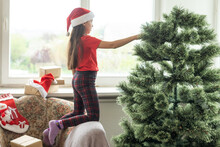 Photo Of Cute Cheerful Little Girl Makes An Artificial Christmas Tree Wear Santa Hat Indoors
