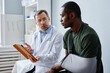 © Seventyfour - Mature Caucasian doctor telling young African American military officer about broken arm treatment