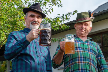 Wall Mural - Senior men with beer mugs with Bavarian beer in Tyrolean hats celebrating a beer festival in Germany. Happy old people during the October holiday in Munich