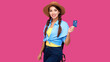 © khmelev - Smiling caucasian female student holding credit card on vivid pink isolated background. Young woman traveler with backpack