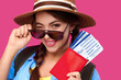 © khmelev - Smiling caucasian woman insunglasses holding passport with travel ticket inside over pink isolate background. Studoi shot