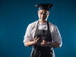 Man cook with phone. Guy in chef's uniform cook of restaurant on dark background. Career in restaurant concept. Indian restaurant owner. Chef in black cook hat. Cafe employee. Human confectioner