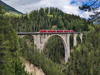 Wiesener Viaduct in the Davos mountains near Filisur. Beautiful old stone bridge with a moving train. Spring Time