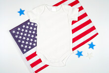 Baby Romper Onesie Bodysuit Jumpsuit Product Mockup. Patriotic Fourth Of July, Independence Day Theme Craft Product Mockup Styled With USA Stars And Stripes Flag Against A White Background.