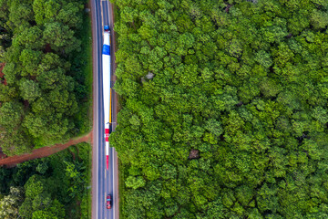 Aerial view of long vehicle truck with special semi-trailer for transporting oversized load or exceptional convoy through a rural forest and mountainous area. Transportation and logistics concept