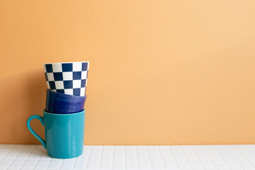 Wall Mural - Stack of blue cups on white table. orange wall background. copy space