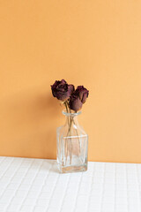 Wall Mural - Vase of red dry rose flowers on white table. orange wall background. copy space