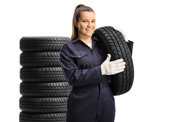 Wall Mural - Pile of tires and a young female mechanic worker carrying a tire