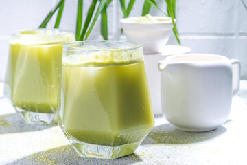 Cold matcha green tea drink. Iced matcha latte cocktail in two glasses with summer tropical palm leaves on white background copy space