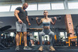 Leinwandbild Motiv Front full body indoor shot of two caucasian people at gym - a male trainer and a sports girl - training weightlifting with small barbell. High quality photo