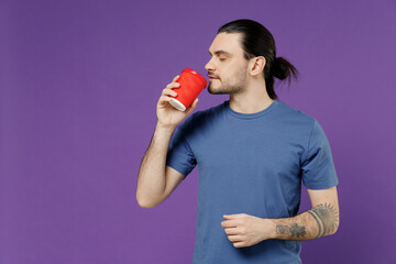 Young man 20s wear basic blue t-shirt with blank print design hold takeaway delivery craft paper brown cup coffee to go sniff scent enjoying isolated on plain purple color background studio portrait