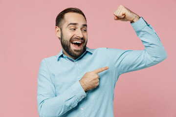 Wall Mural - Young excited strong sporty fitness man 20s wear classic blue shirt showing point finger on biceps muscles on hand demonstrating strength power isolated on plain pastel light pink background studio