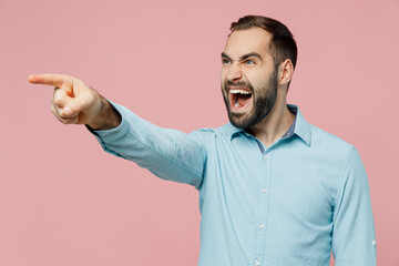 Wall Mural - Young angry indignant strict sad caucasian man 20s wearing classic blue shirt point index finger aside scream isolated on plain pastel light pink background studio portrait. People lifestyle concept.