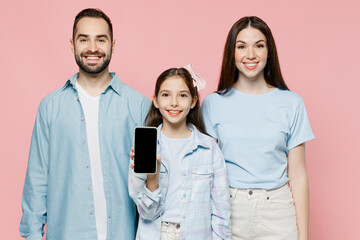 Wall Mural - Young happy parents mom dad with child kid daughter teen girl in blue clothes hold in hand use mobile cell phone with screen workspace area isolated on plain pastel pink background Family day concept