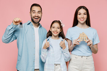 Wall Mural - Young happy excited cool fun smiling parents mom dad with child kid daughter teen girl in blue clothes hold keys wooden house mockup isolated on plain pastel light pink background. Family day concept.