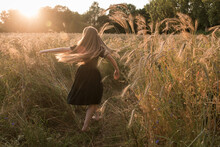 Young Woman In Dress Running In Of Grass And Grain At Sunset In Summer