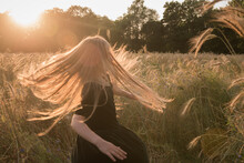 Girl In Dress Dancing And Twirling In Field Of Grain At Sunset In Summer
