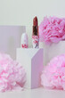Lipstick on a white background with architecture shapes and pink flowers.Close up on lipstick in deep nude color in in white packaging with cherry blossom