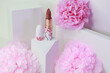 Lipstick on a white background with architecture shapes and pink flowers.Close up on lipstick in deep nude color in in white packaging with cherry blossom