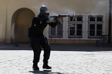 Człowiek z karabinem kałasznikow w czarnym ubiorze idzie ulicą.