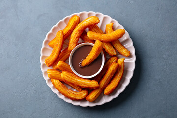 Wall Mural - Churros dessert with chocolate sauce, dip, topping on white plate. Gray background. Close up. Top view.