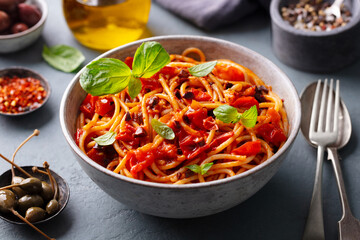 Wall Mural - Pasta, spaghetti with tomato sauce, olives and fresh basil. Puttanesca recipe. Grey background. Close up.