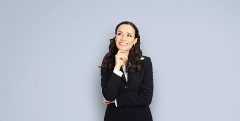 Sticker - Happy smiling amazed positive businesswoman looking up, with copy space for slogan or text. Confident brunette woman in black suit, isolated over grey background. Business concept image.