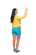 Back view of young casual female in full length pointing at blank copy space