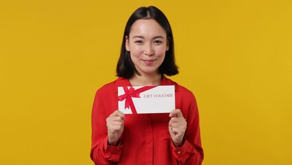 Wall Mural - Surprised shocked happy young woman of Asian ethnicity 20s wear red shirt pointing finger on gift certificate voucher for store doing winner gesture isolated on plain yellow background studio portrait