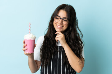 Young woman with strawberry milkshake isolated on blue background looking to the side and smiling