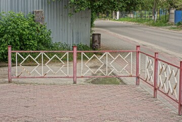 Wall Mural - red white metal decorative fence made of twigs on a sidewalk near an asphalt road