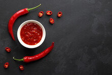 Chili Sauce In A Bowl Along With Chilli Peppers On A Dark Slate Surface With Copy Space. Top View