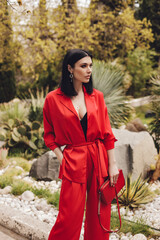 Wall Mural - beautiful woman with dark hair in elegant red suit posing in summer park