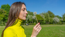 Beautiful Young Woman Blowing A Dandelion. Girl With Dandelion In Hand. Allergic To Pollen Of Flowers. Spring Allergy.