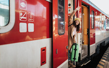 Happy Young Traveler Woman With Luggage Getting In The Train At Train Station Platform