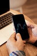 © Evgeniya Grande - Closeup man hands holding phone, analysing investment charts on display and working with laptop