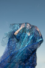 Art Portrait Under Blue Sky Of Woman In A Dress And Shiny Fabric